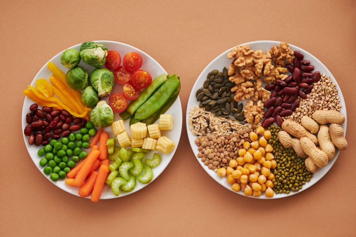 Zwei Teller von oben auf orangem Grund, links buntes Gemüse wie Brokkoli, Tomaten, Karotten und Erbsen, rechts Hülsenfrüchte, Nüsse und Samen