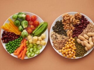 Zwei Teller von oben auf orangem Grund, links buntes Gemüse wie Brokkoli, Tomaten, Karotten und Erbsen, rechts Hülsenfrüchte, Nüsse und Samen