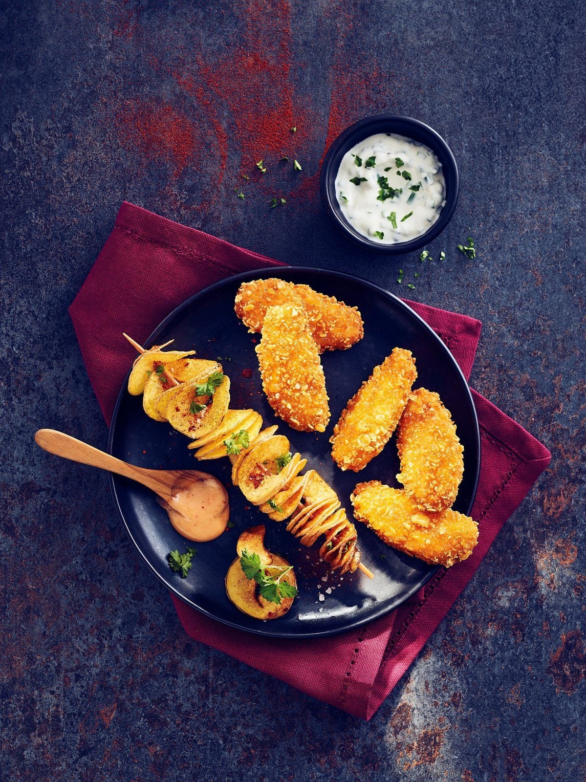 Teller mit panierten pflanzlichen Tenders und Kartoffelspießen, daneben ein Dip