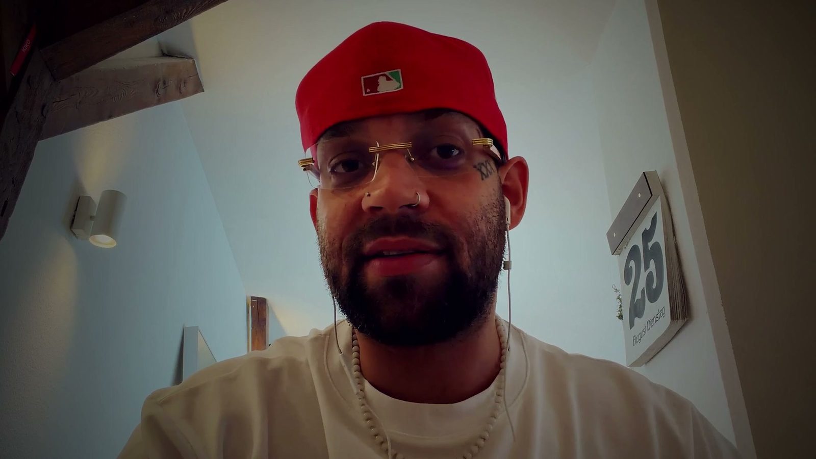 FAYAN mit roter Cap und randloser Brille spricht in die Kamera, hinter ihm eine Dachschräge