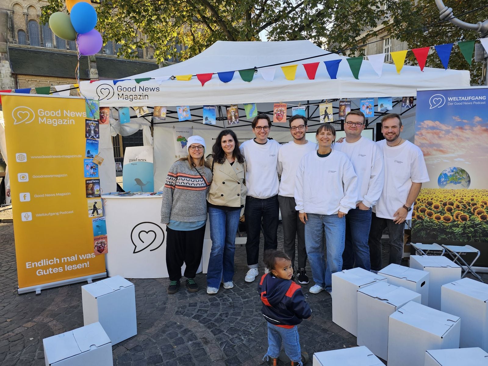 Team des Good News Magazins vor seinem Stand mit Wimpelkette bei einer Veranstaltung