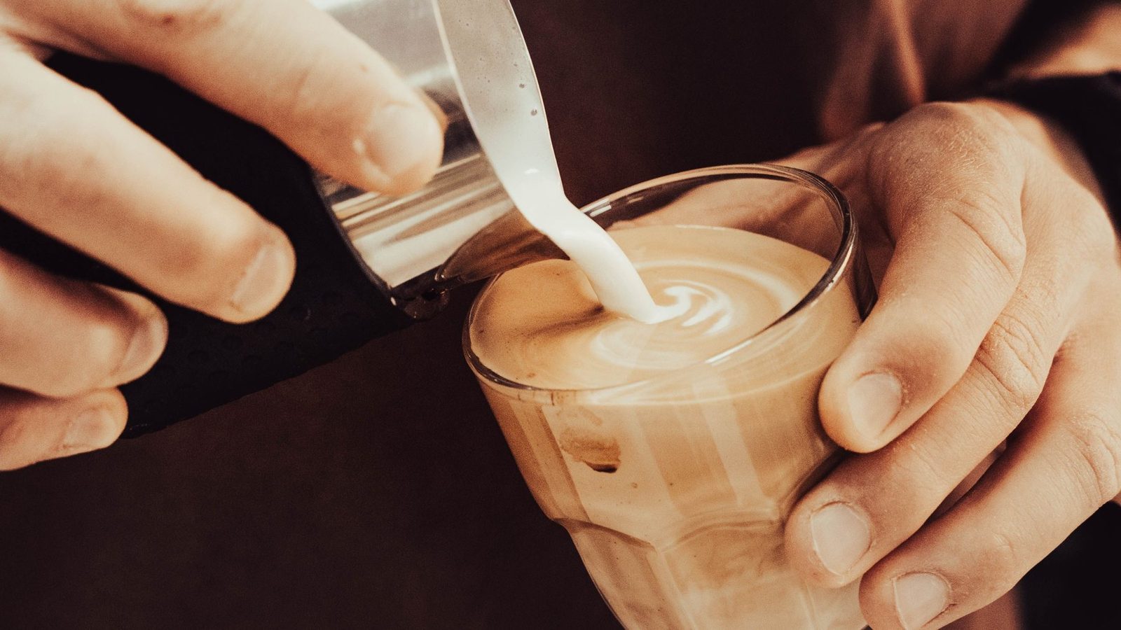 Barista gießt aufgeschäumten Milchschaum in eine Tasse und formt dabei Latte Art