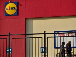 Lidl-Filiale mit Logo an der roten Fassade, davor zwei Passanten