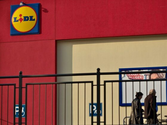 Lidl-Filiale mit Logo an der roten Fassade, davor zwei Passanten