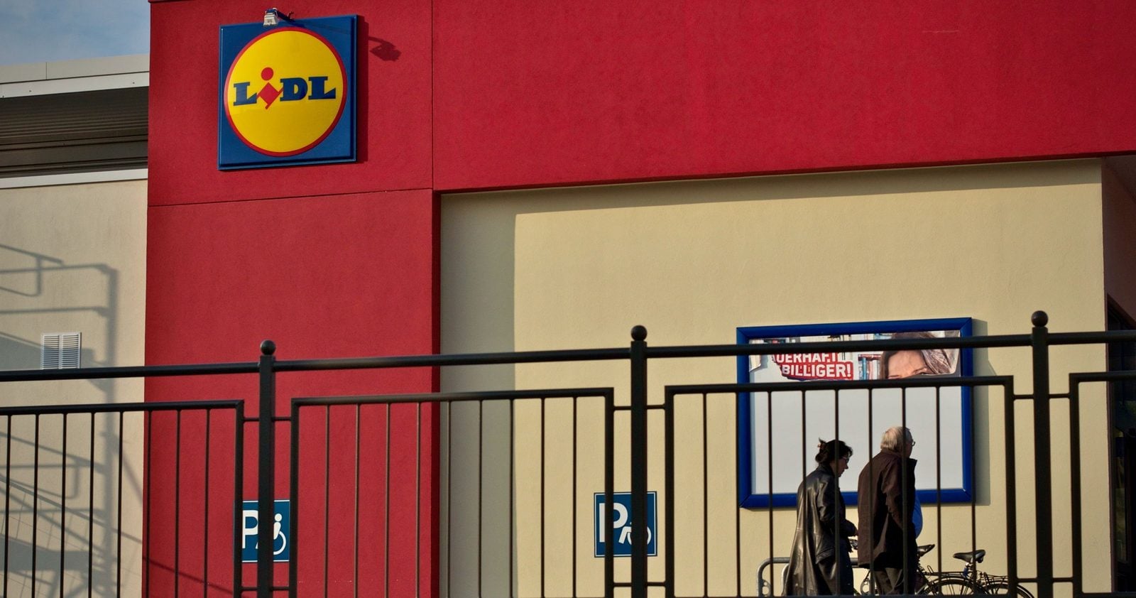 Lidl-Filiale mit Logo an der roten Fassade, davor zwei Passanten