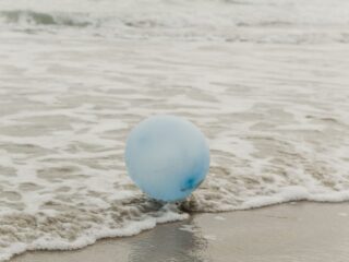 Ein hellblauer Luftballon liegt am Strand in der Brandung