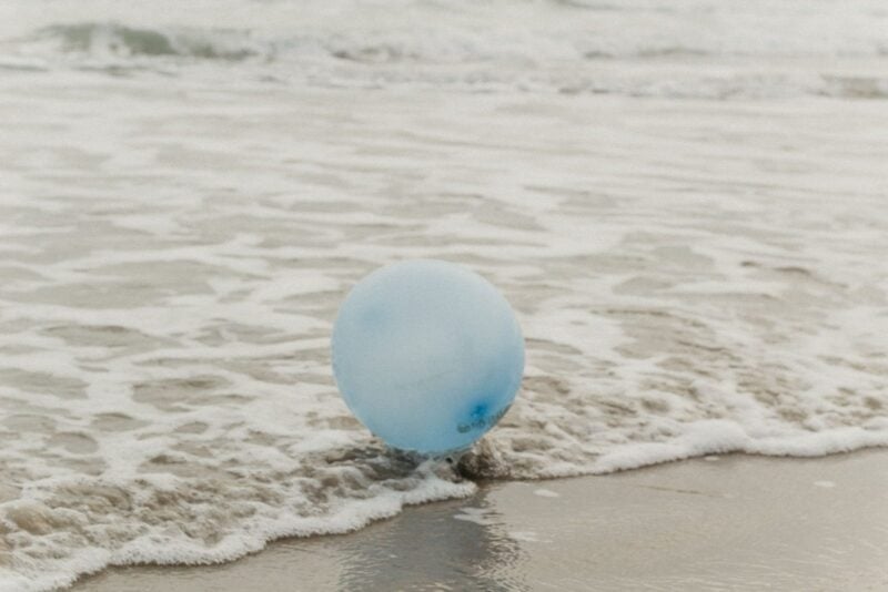 Ein hellblauer Luftballon liegt am Strand in der Brandung