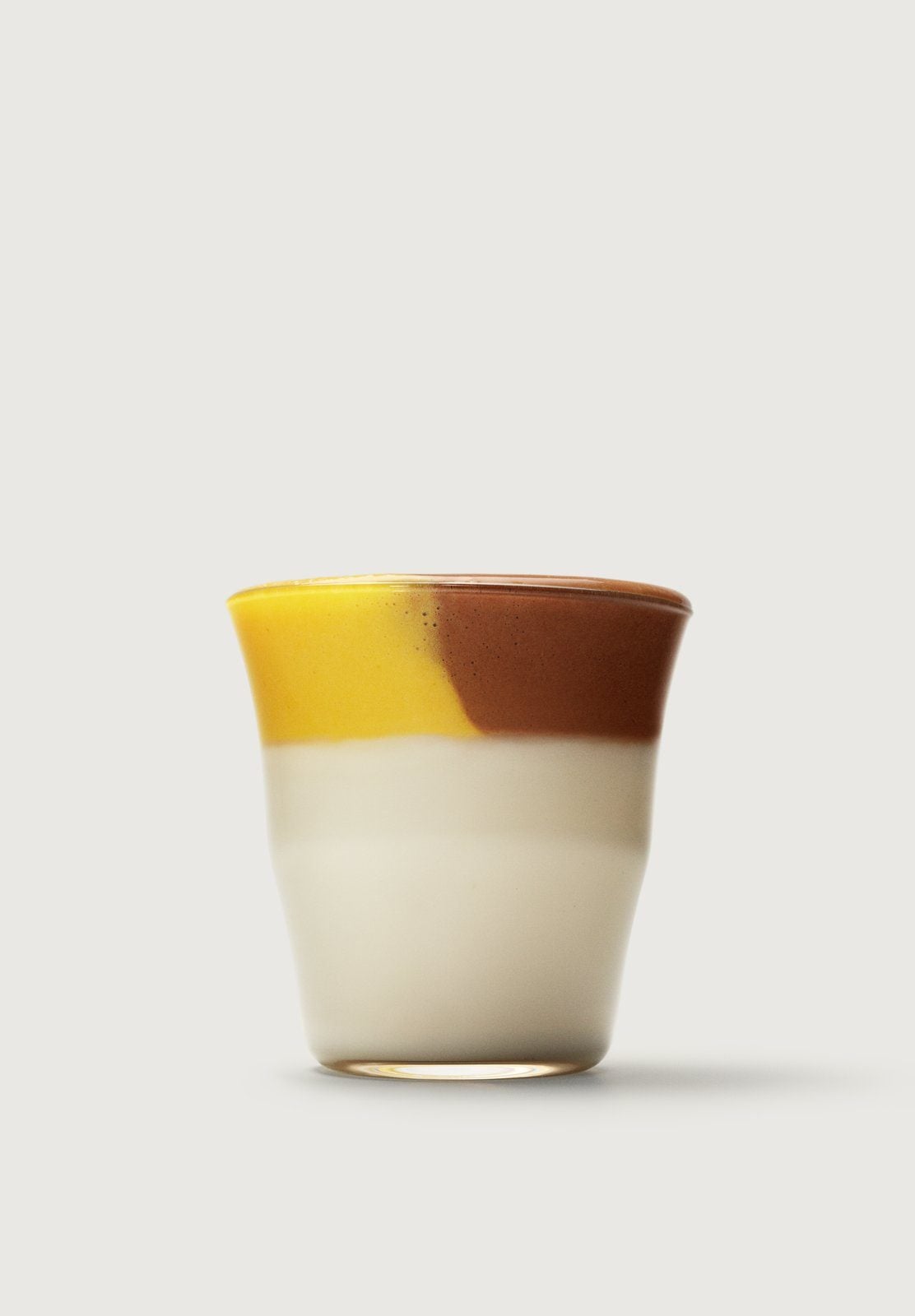 Ein Drink in drei Schichten aus Weiß, Gelb und Schokoladenbraun in einem Glas