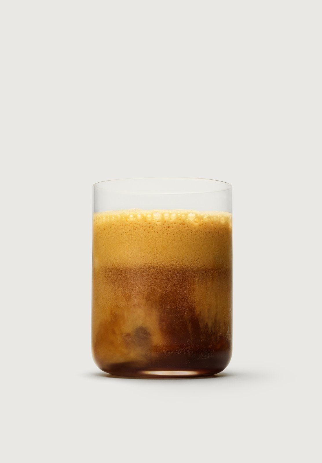 Ein geshakter Espresso mit Orange und Safran, darauf hellbrauner Schaum, in einem Glas