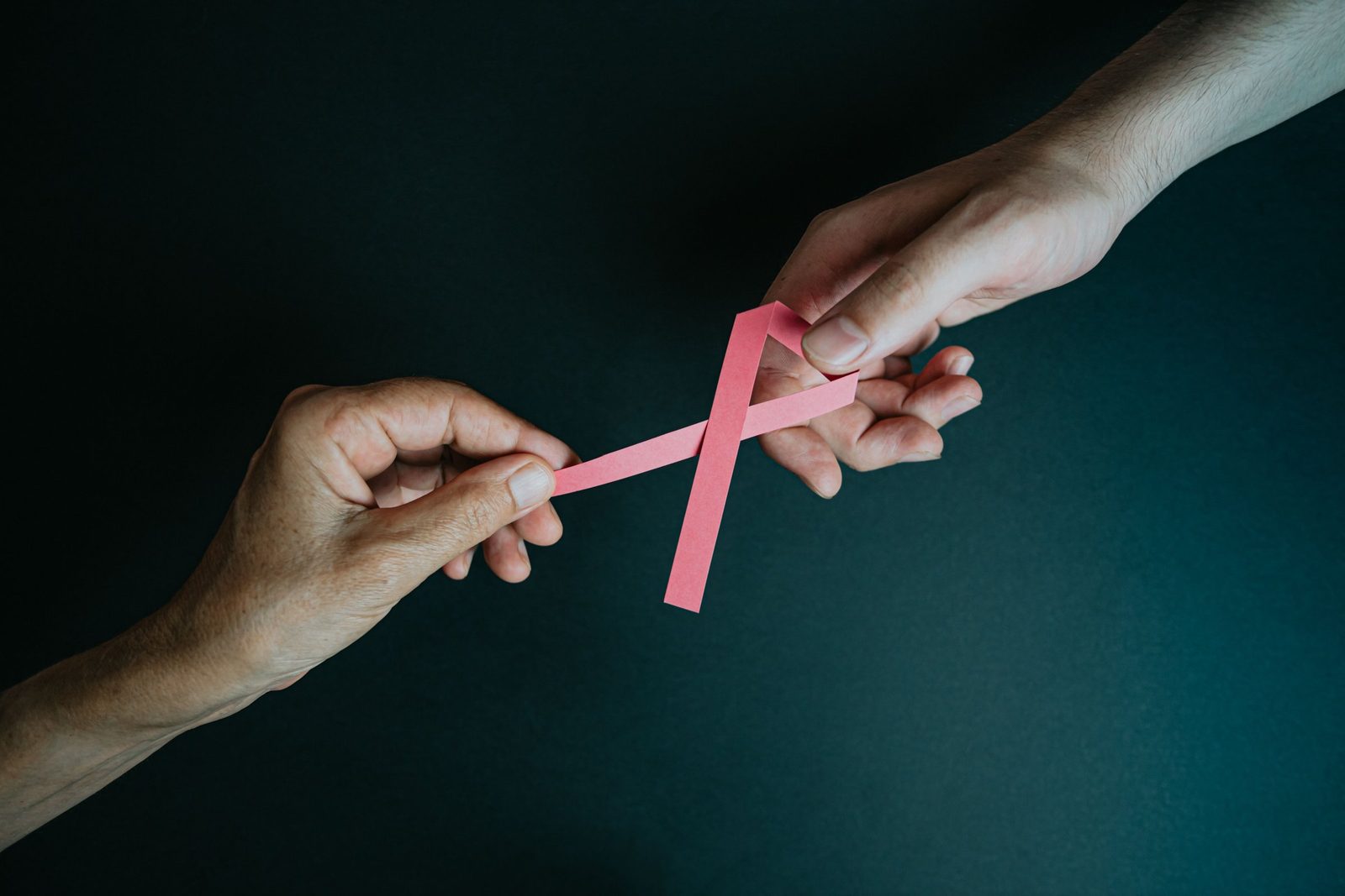 Zwei Hände reichen sich eine rosa Schleife als Symbol für Brustkrebs-Aufklärung