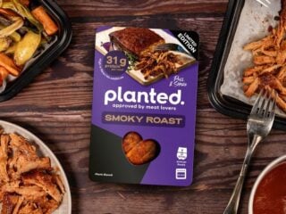 Packung planted Smoky Roast Limited Edition auf einem Holztisch mit gezupftem Braten, Ofengemüse und Soße