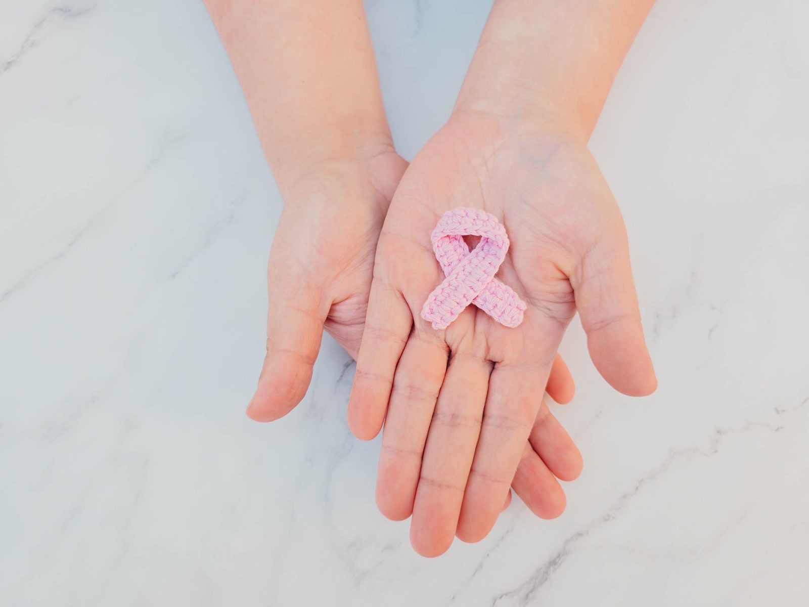 Hände halten eine kleine rosa Schleife