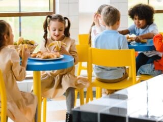 Kinder essen an bunten Tischen in einer Schulmensa zu Mittag