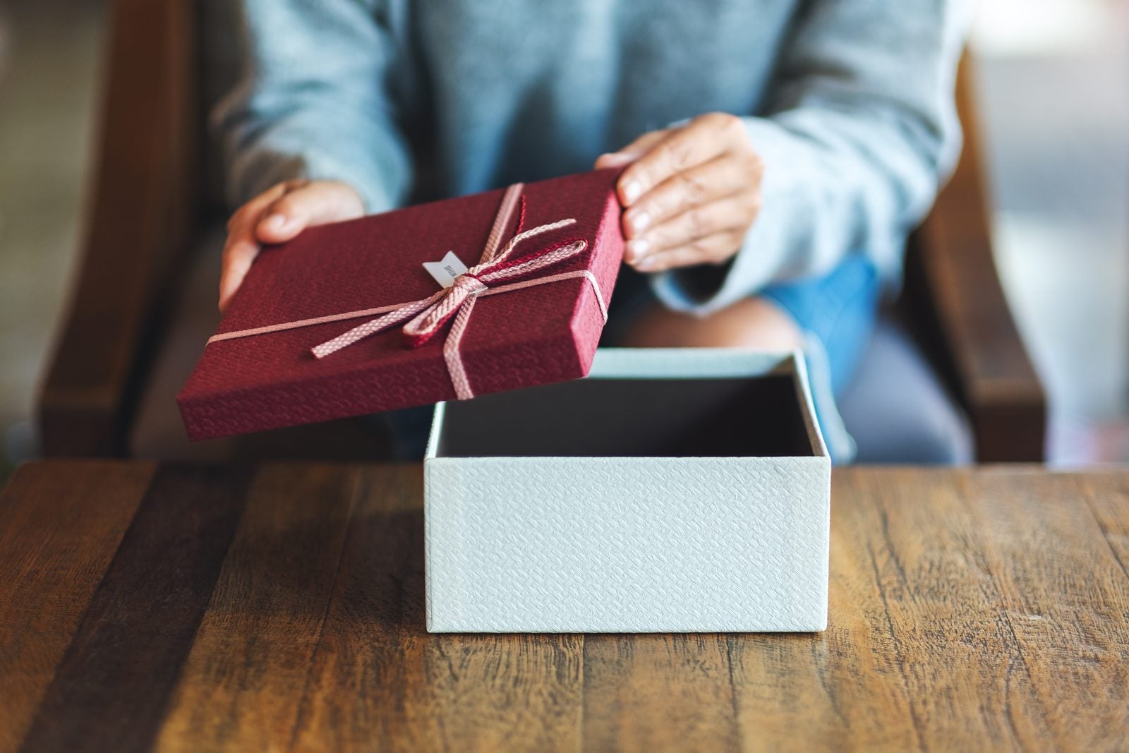Hände heben den Deckel von einer Geschenkbox
