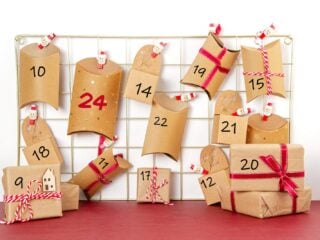 Selbstgemachter Adventskalender aus Kraftpapier-Schachteln mit Zahlen und roten Schleifen an einem Metallgitter