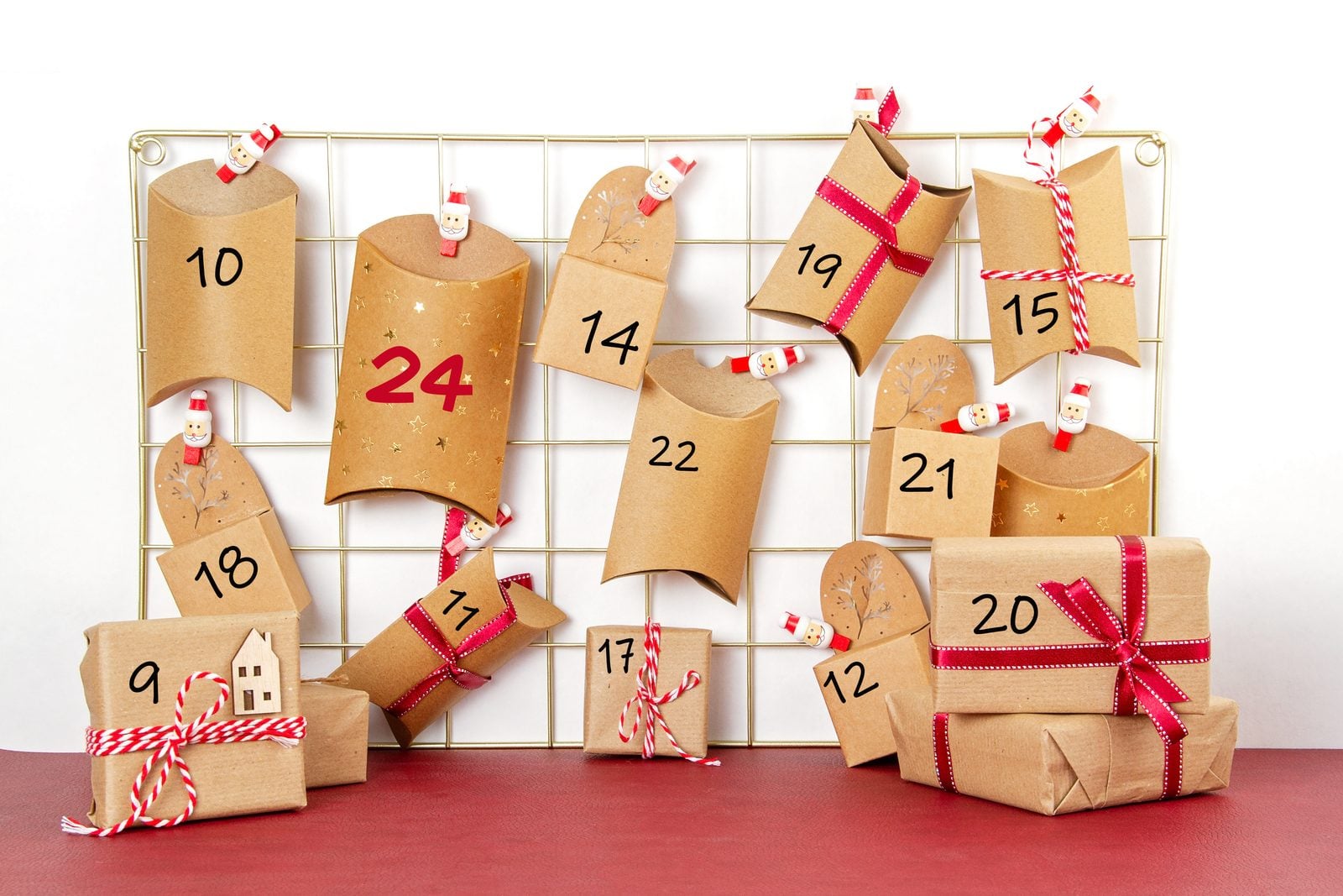 Selbstgemachter Adventskalender aus Kraftpapier-Schachteln mit Zahlen und roten Schleifen an einem Metallgitter