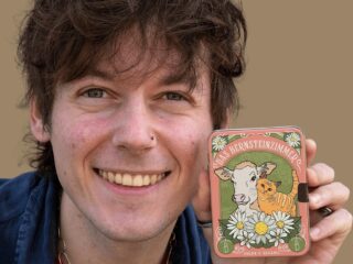 Tobias Wille alias Vegan Veteran hält lächelnd die Pralinendose von Das Bernsteinzimmer