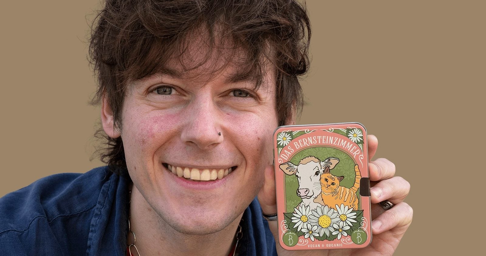 Tobias Wille alias Vegan Veteran hält lächelnd die Pralinendose von Das Bernsteinzimmer
