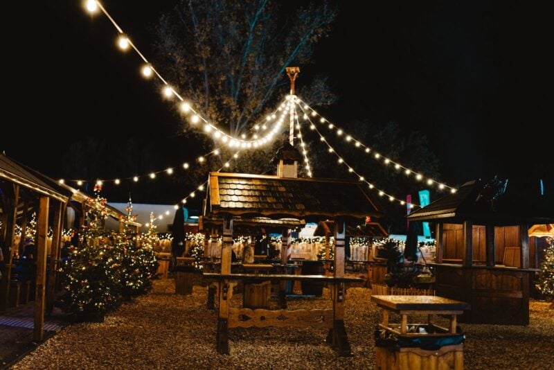 Symbolbild: Holzhütten eines Weihnachtsmarkts unter Lichterketten am Abend