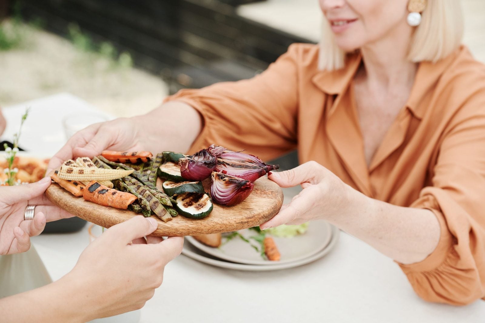 Eine Person reicht eine Platte mit gegrilltem Gemüse über einen gedeckten Tisch