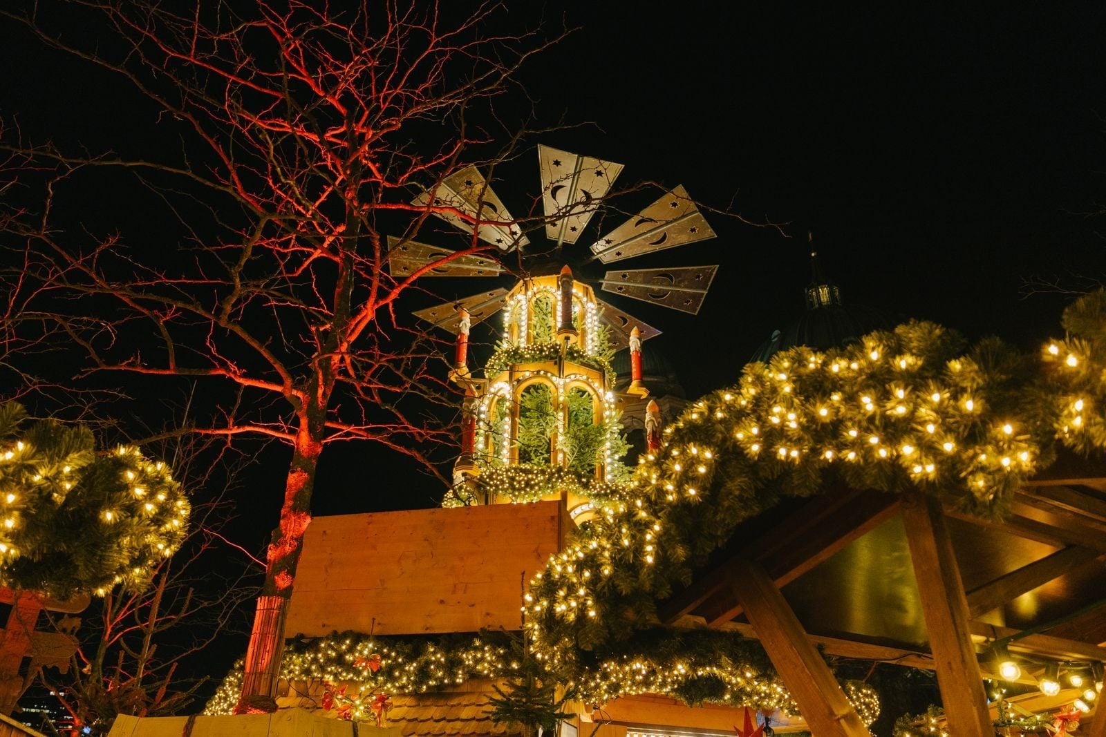 Symbolbild: Weihnachtspyramide mit Lichtergirlanden und beleuchtetem Baum am Abend