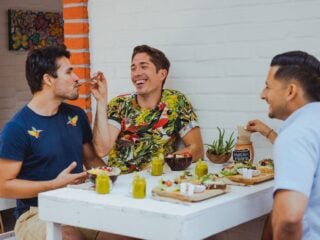 Vier Freunde essen gemeinsam in einem veganen Café, an der Wand ein Schild mit Vegan is Life