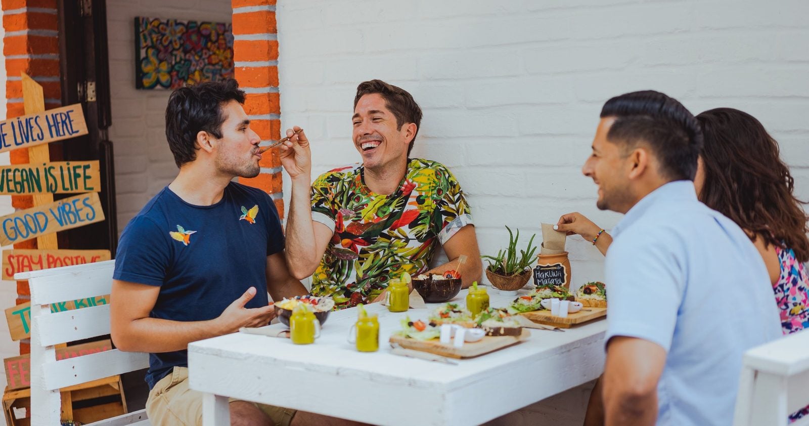 Vier Freunde essen gemeinsam in einem veganen Café, an der Wand ein Schild mit Vegan is Life