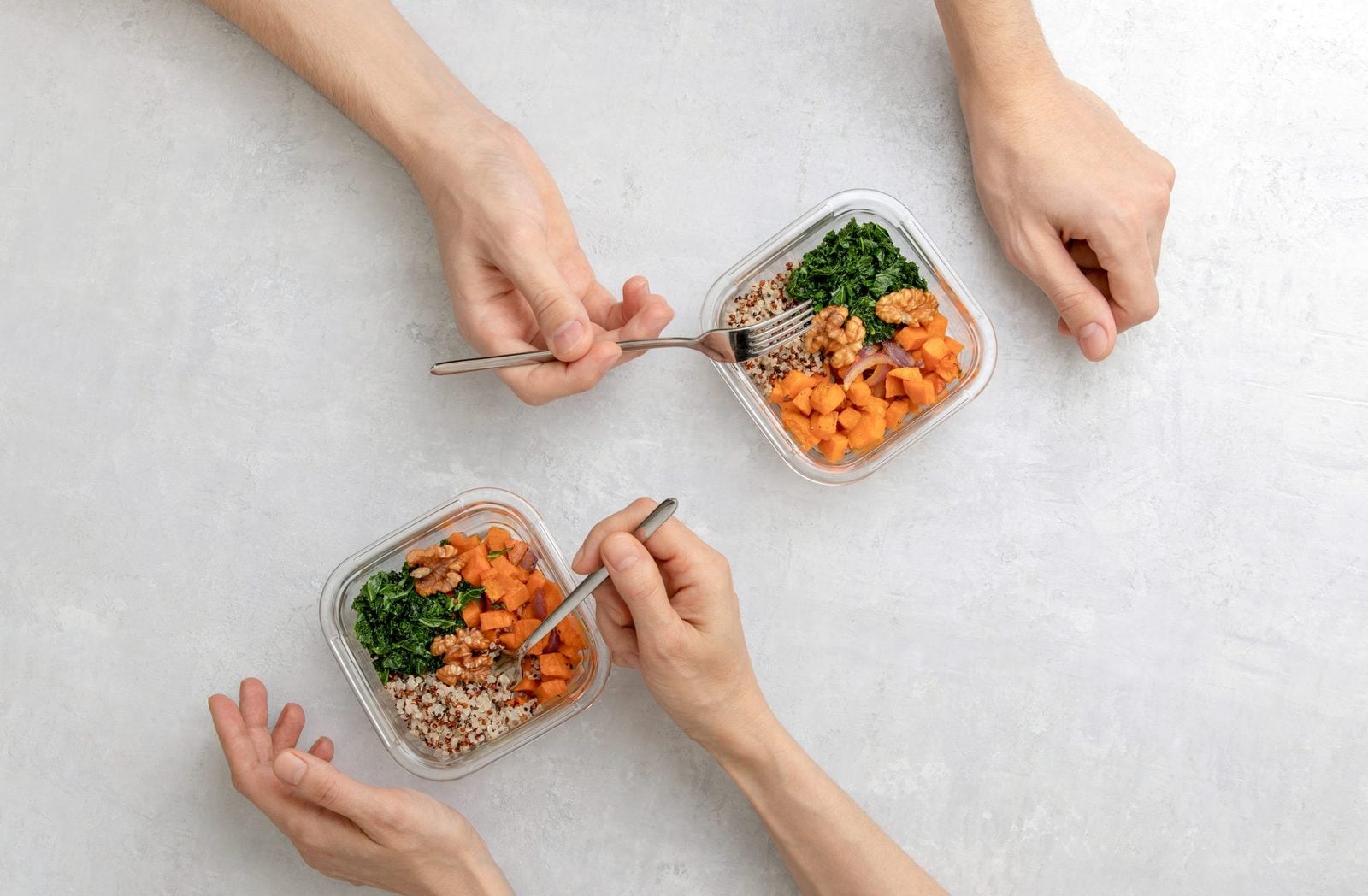 Zwei Personen essen von oben gesehen aus Glasdosen mit Ofengemüse, Grünkohl, Walnüssen und Quinoa
