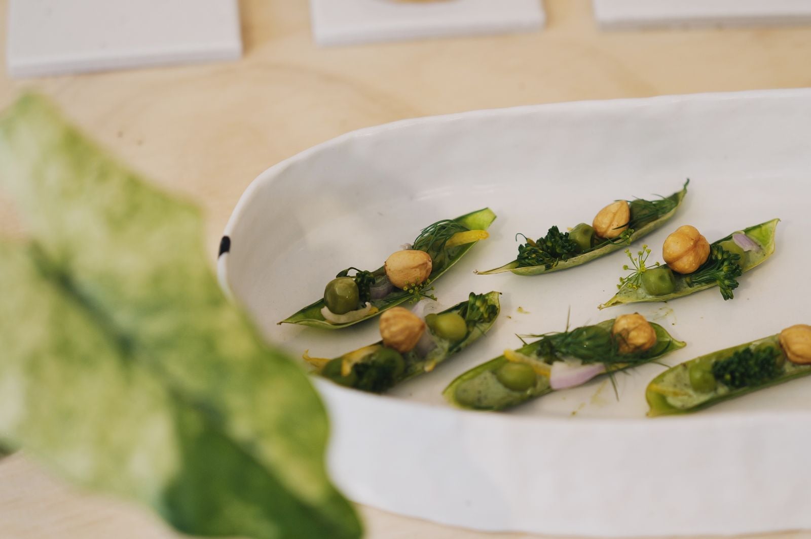 Angerichtete Zuckerschoten mit grüner Kräutercreme, Erbsen, Haselnüssen und Dill in einer weißen Keramikschale