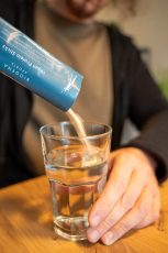 Veganes Proteinpulver wird in ein Glas Wasser gegossen, ideal für eine pflanzliche Ernährung.