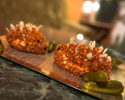 Vegane Mett angerichtet auf einer Vesperplatte mit Zwiebeln darauf verteilt und Essiggurken daneben